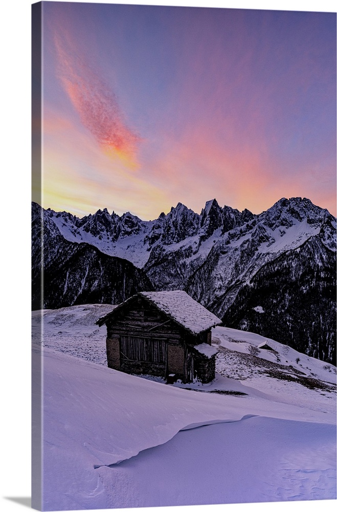 Lone mountain hut in deep snow with majestic peaks in the background at dawn, Tombal, Val Bregaglia, Graubunden, Switzerla...