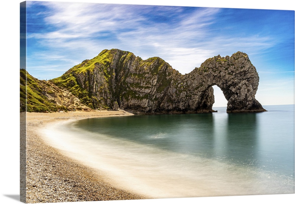 Scenic view of a natural arch on a coastline with a sandy beach and clear blue sky at Durdle Door, Jurassic Coast, UNESCO ...