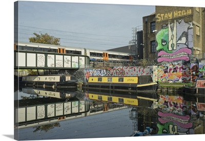 Overground train drives past canal by artists studios and warehouses in Hackney Wick