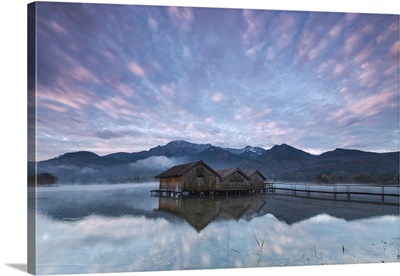 Pink clouds and wooden huts are reflected in the clear water of Kochelsee, Germany