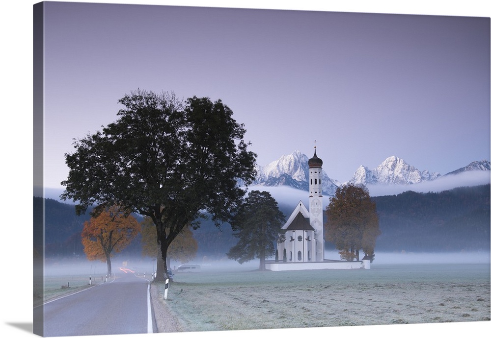 Pink sunrise and mist of autumn on St. Coloman Church framed by snowy peaks, Schwangau, Bavaria, Germany