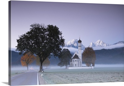 Pink sunrise and mist of autumn on St. Coloman Church framed by snowy peaks