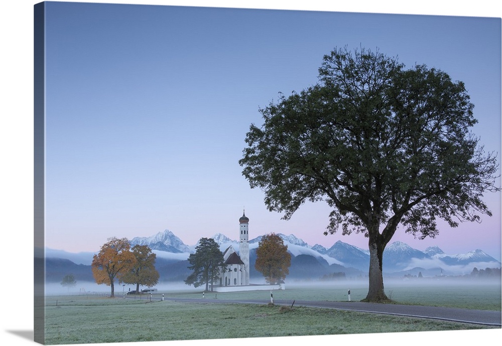 Pink sunrise and mist of autumn on St. Coloman Church framed by snowy peaks, Schwangau, Bavaria, Germany