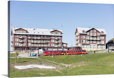 Red wagons of Wengernalpbahn rack railway run next to alpine hotels, Switzerland