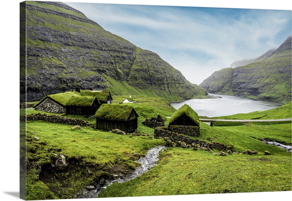 River flowing to the ocean crossing green meadows with grass-roof houses, Saksun, Streymoy Island, Faroe Islands, Denmark,...