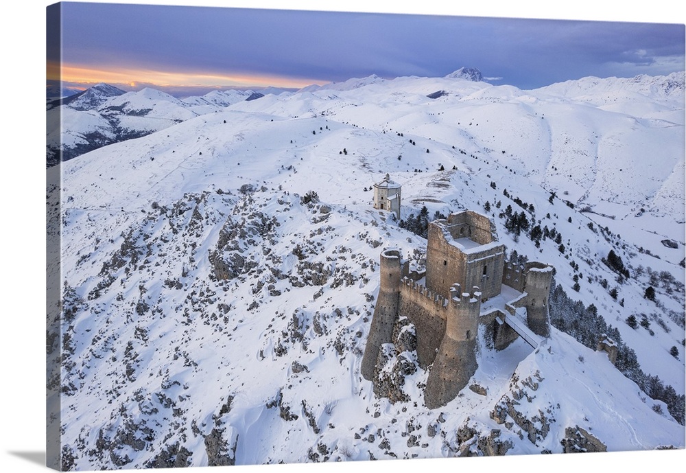 Aerial winter view of Rocca Calascio castle and the Santa Maria della Pieta church in the snowy landscape at dusk, Campo I...