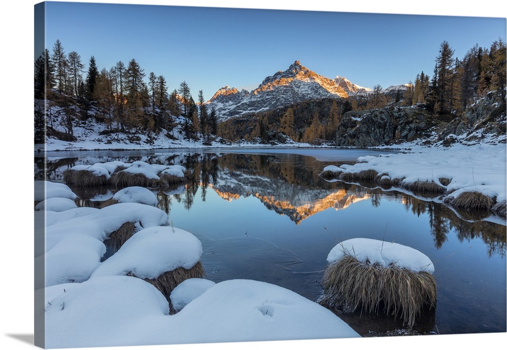 The rocky peak reflected in the frozen Lake Mufule at dawn, Malenco Valley, Province of Sondrio, Valtellina, Lombardy, Italy