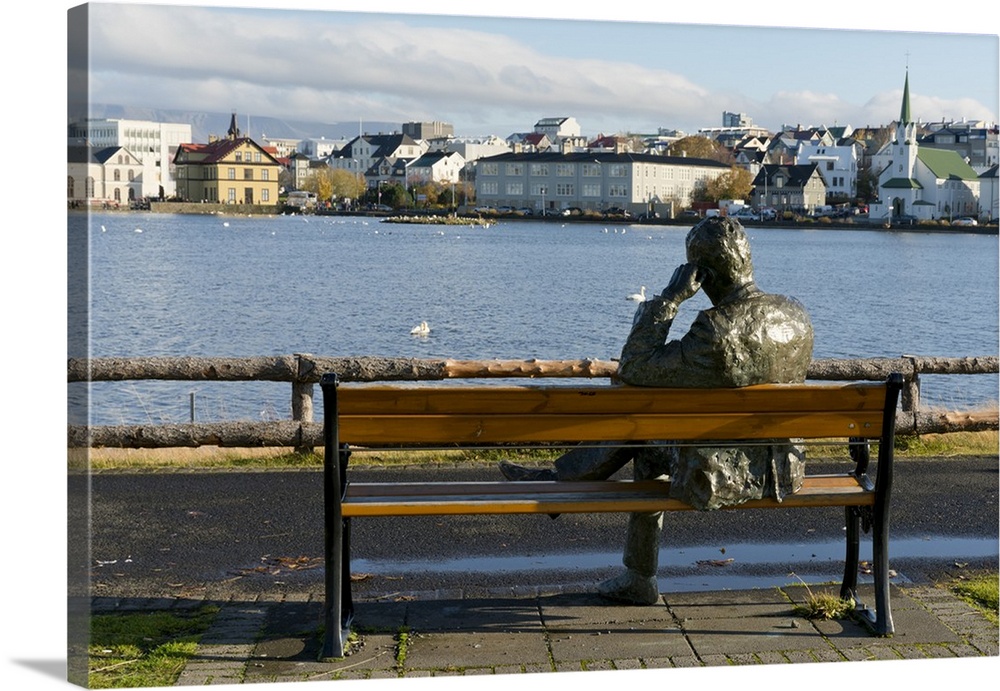 Sculpture of a man sitting on a park bench in front of Tjornin Lake and the Historic Centre of Rykjavik, Iceland, Polar Re...