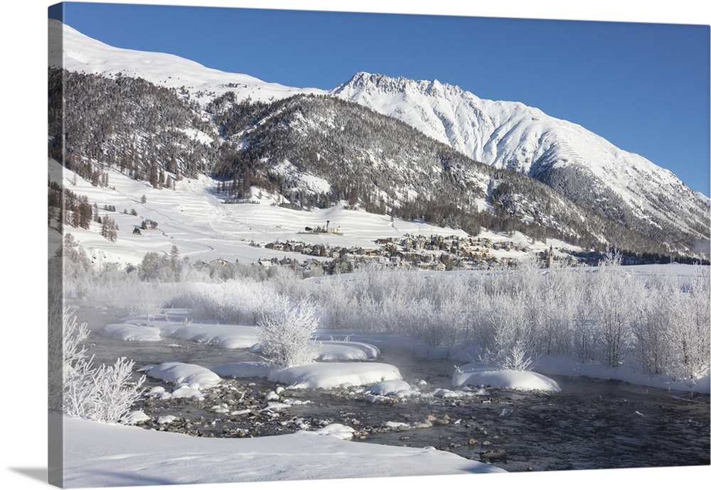 Snow covered trees and river Inn frame the alpine village of Samedan, Maloja, Canton of Graubunden, Engadine, Switzerland,...