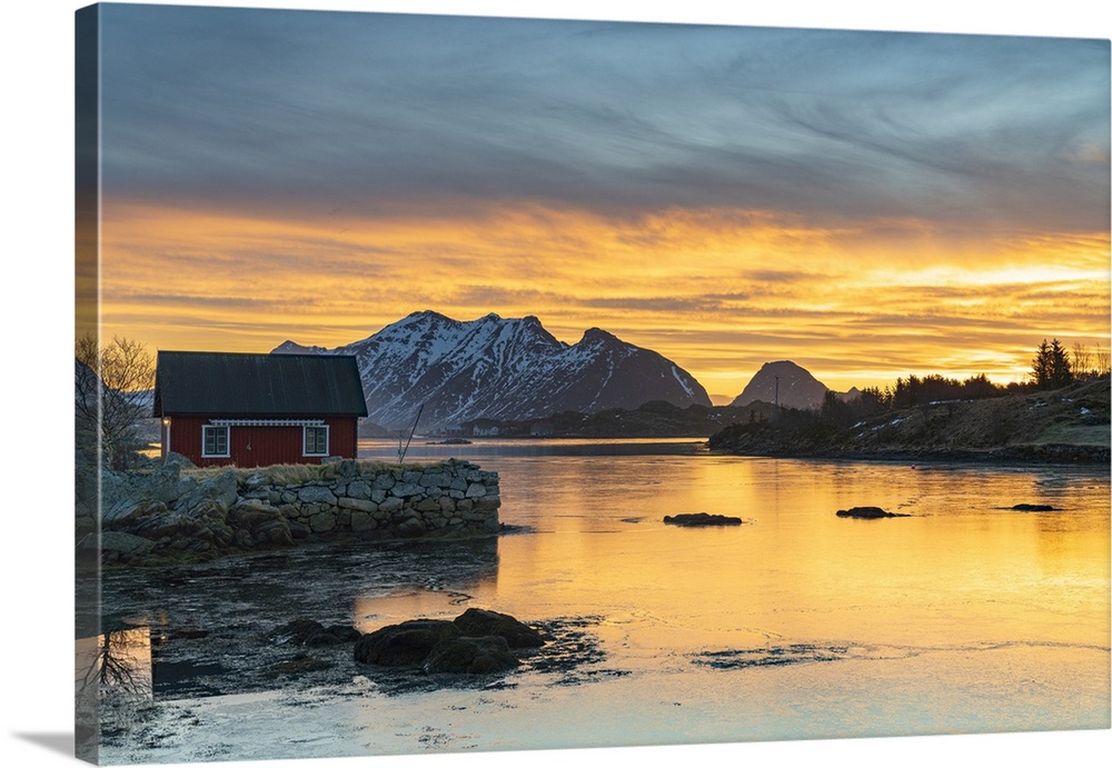 Snowcapped mountains and fisherman's red cabin under the burning sky at dawn, Ballstad, Vestvagoy, Lofoten Islands, Norway...