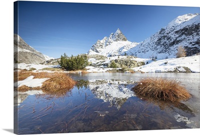 Snowy peaks are reflected in the alpine lake partially frozen, Engadine, Switzerland