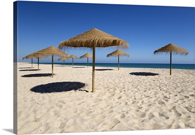 Straw umbrellas on empty white sand beach with clear sea behind