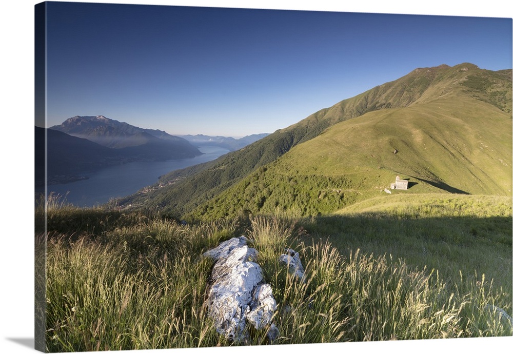 Sunbeam on Church of San Bernardo lights up the landscape around the blue water of Lake Como at dawn, Musso, Lombardy, Ita...