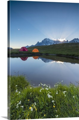 Tents in the green meadows surrounded by flowers and alpine lake, Mont De La Saxe, Italy