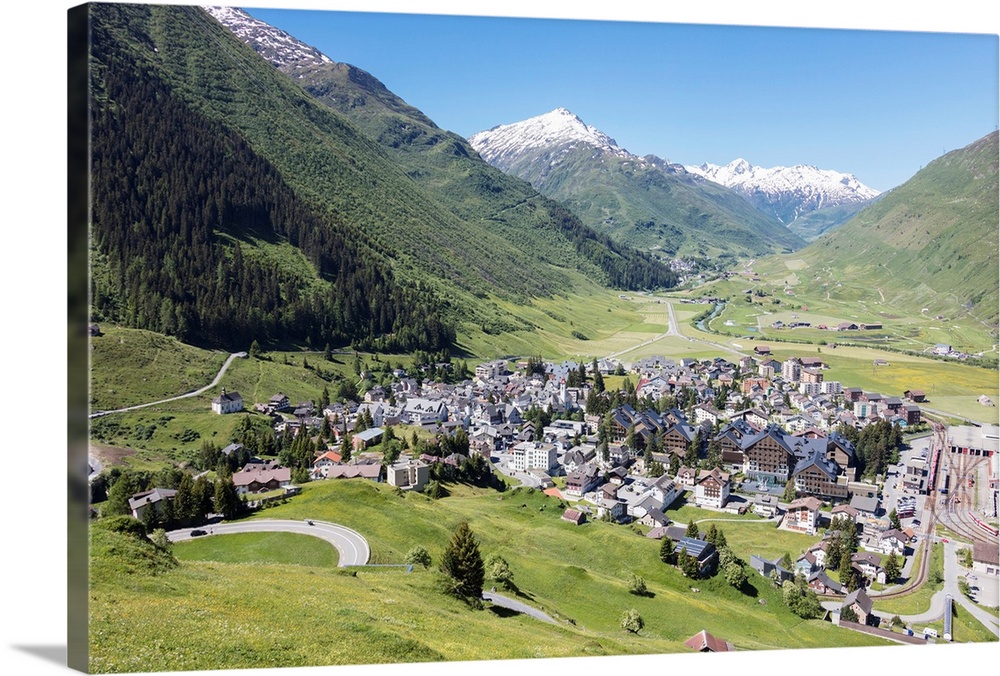 The alpine village of Andermatt surrounded by green meadows, and snowy peaks in the background, Canton of Uri, Switzerland...