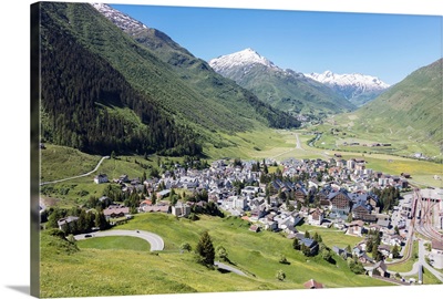 The alpine village of Andermatt surrounded by green meadows and snowy peaks behind