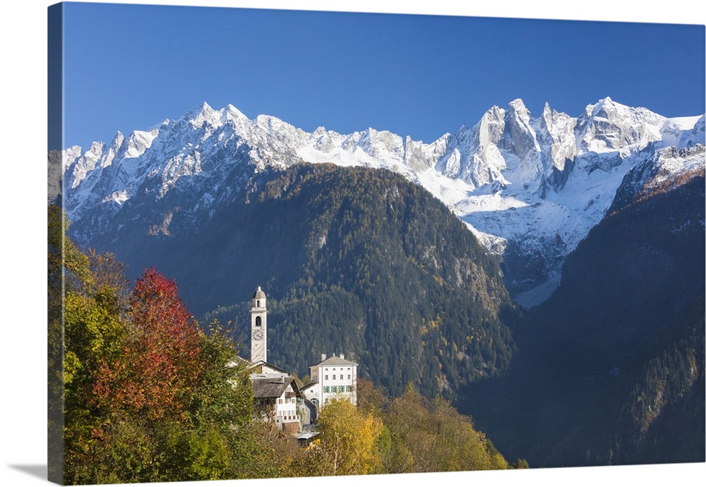 The colorful trees frame the alpine church and the snowy peaks, Soglio, Bregaglia Valley, Canton of Graubunden, Swiss Alps...