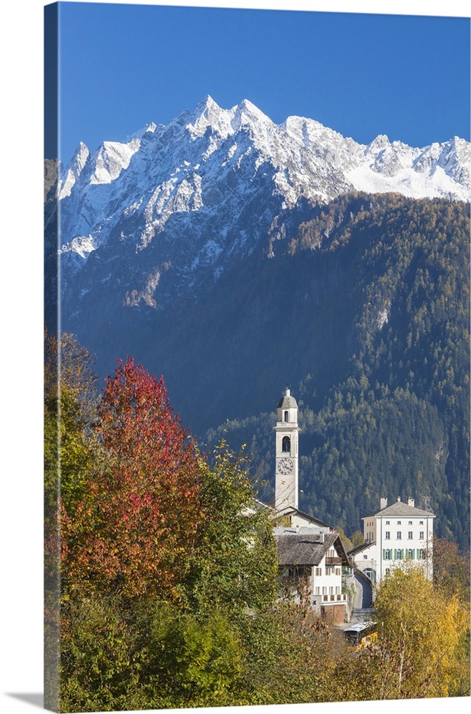 The colorful trees frame the alpine church and the snowy peaks, Soglio, Bregaglia Valley, Canton of Graubunden, Swiss Alps...