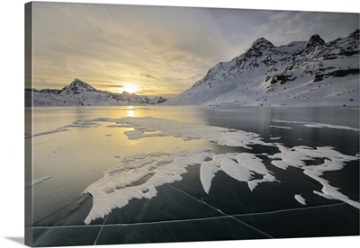 The frozen surface of Lago Bianco framed by snowy peaks at dawn, Engadine, Switzerland