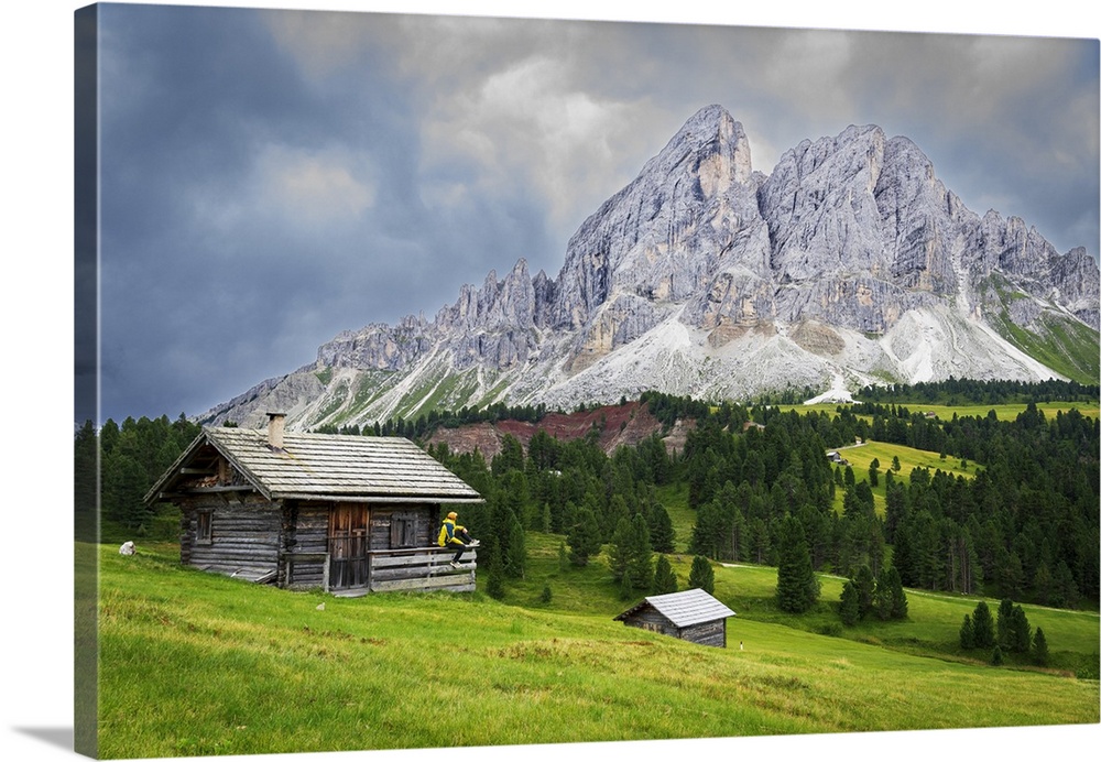 Side view of a hiker on chalet in green meadows admiring the rocky massif of Sass de Putia, Passo delle Erbe, Dolomites, P...