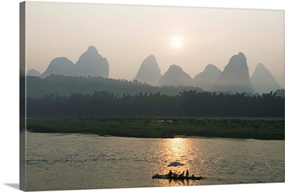 Tourist boat sailing through karst scenery at sunrise on the Li river in Yangshuo, China