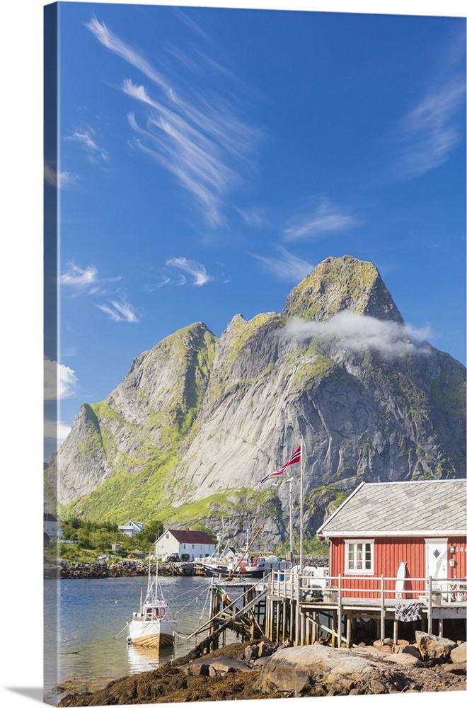 Typical house of fishermen called Rorbu framed by rocky peaks and blue sea, Reine, Moskenesoya, Lofoten Islands, Norway, S...