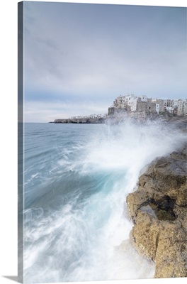 Waves of turquoise sea crashing on cliffs framed by the old town, Apulia, Italy