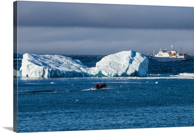 Zodiac cruising back to a cruise ship anchoring behind an iceberg, Antarctica