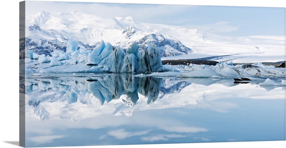 Glacial coastal landscape. Mountains and ice formations reflected in the waters of a glacial lagoon. At lower left, two se...