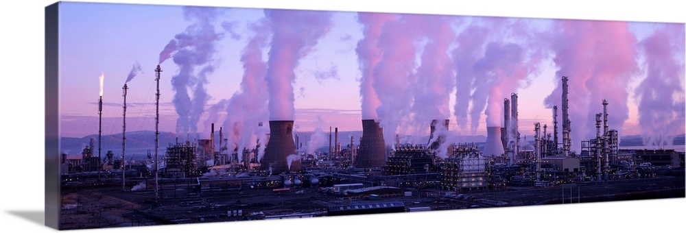 Petrochemical plant at dawn, with clouds of smoke and steam rising from its smokestacks and cooling towers. Flammable gas ...