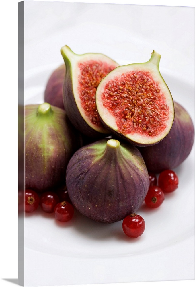 Whole and halved figs on a plate. These fruits are from the fig tree (Ficus carica). The fruits are sweet and edible and c...