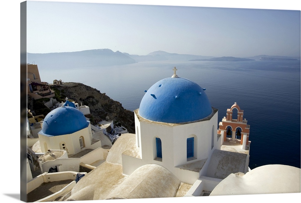 Photograph taken on the coast of Greece looking out toward the water with blue domed churches sitting in the cliffs.