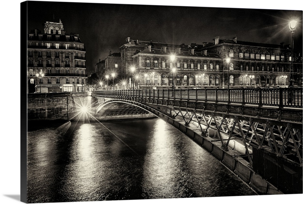 High contrast photograph of a bridge crossing over the Seine River in Paris with lit up buildings in the night sky backgro...