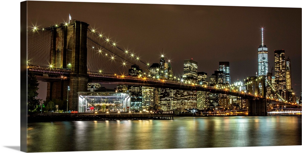 Panoramic photograph of the Brooklyn Bridge illuminated at night, reflected in the water below, with the New York City sky...