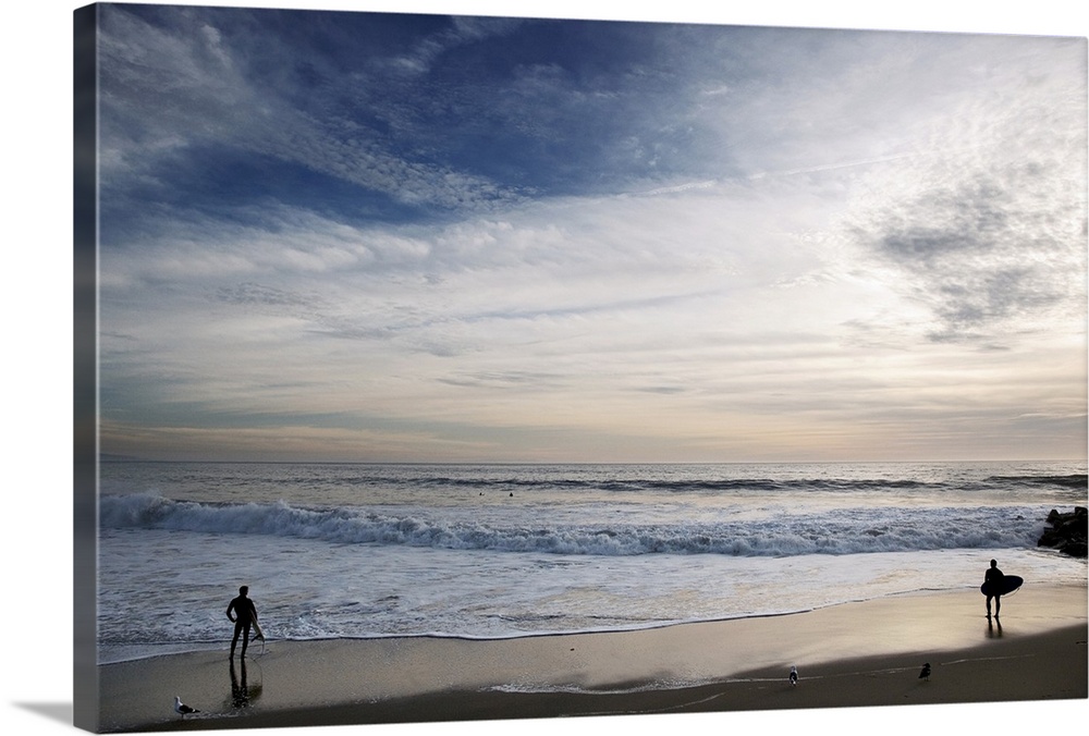 Huge photograph displays a couple individuals with surfboards standing on the edge of the ocean and watching the waves cra...
