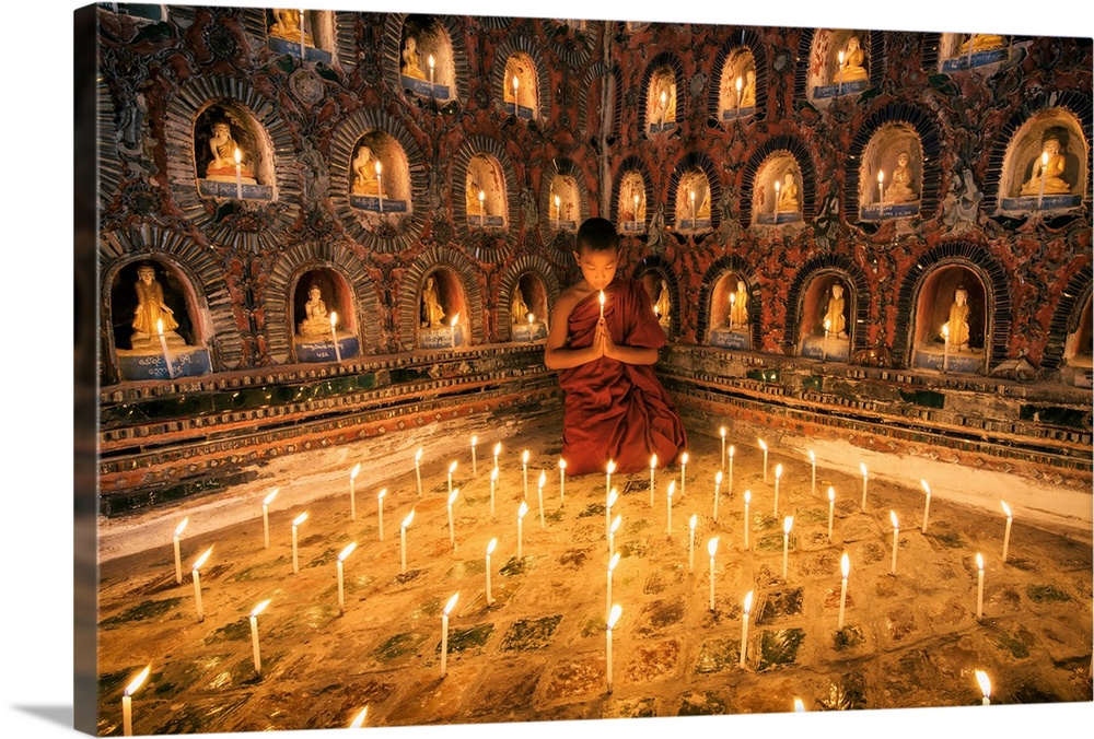 Young monk praying with candles in his monastery in Myanmar.