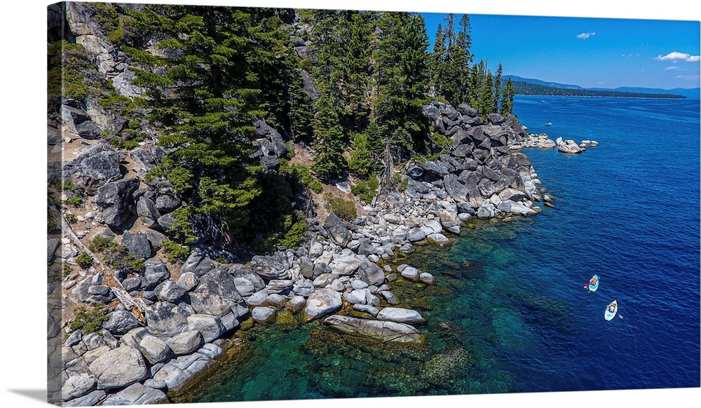 A pair of stand-up paddlers explore beautiful lake Tahoe. Location: Lake Tahoe, California.