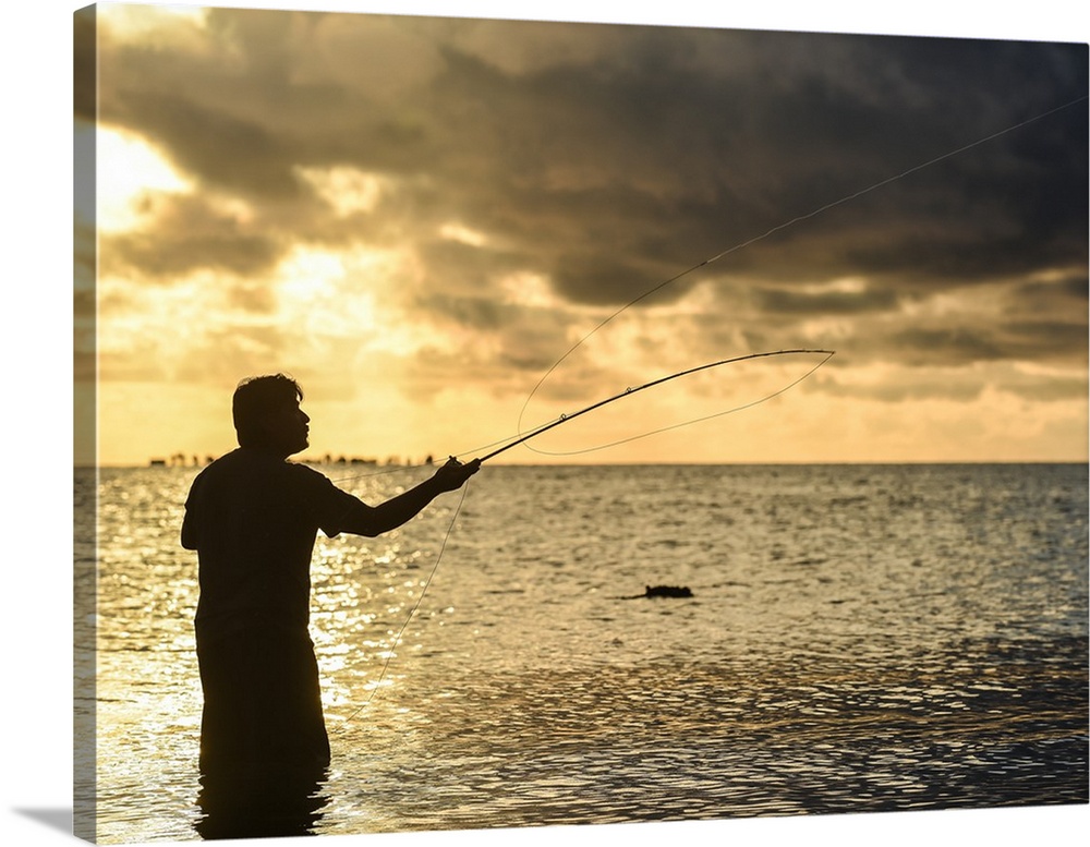 A silhouetted man fly fishing on the beach in Belize at sunset.