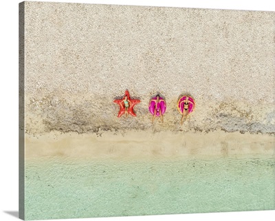 Aerial View Of Three Women Lying On Inflatable Star, Donut, And Flamingo Floats On Beach