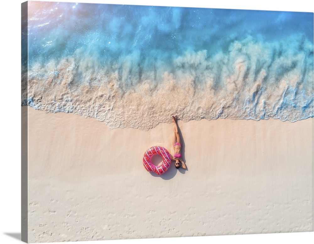 Aerial view of the beautiful young lying woman with pink donut swim ring on the white sandy beach near sea with waves at s...