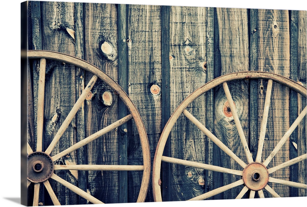 A close up of two vintage wagon wheels lying up against a building.