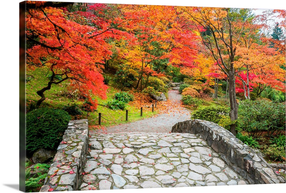 Stone bridge and winding walking path through garden with trees in autumn colors.