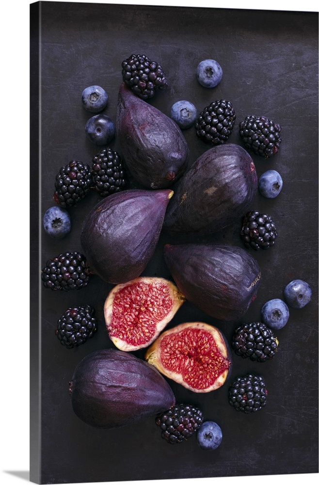 Ripe, purple whole and cut figs, blackberries, and blueberries on black background.