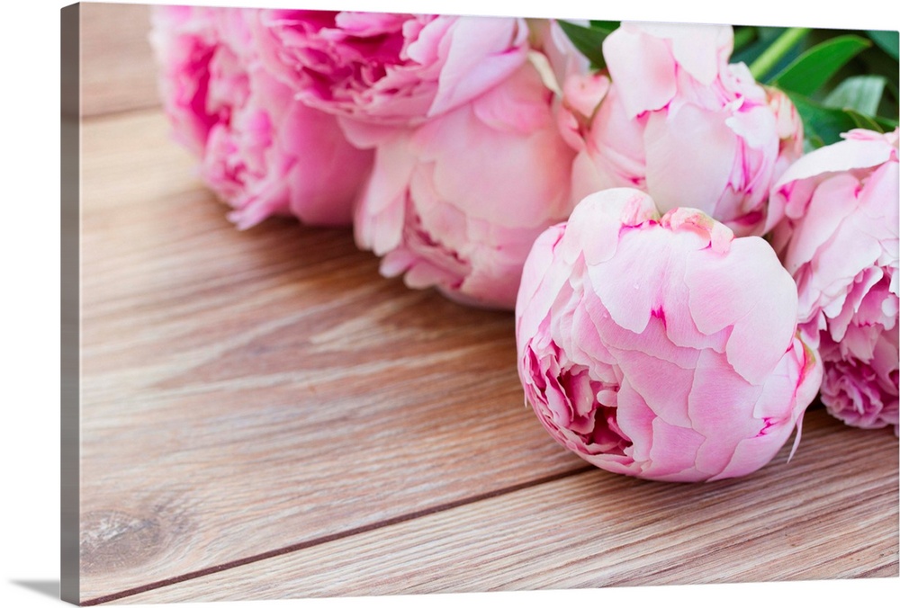 Bouquet of pink peonies laying on wooden table.
