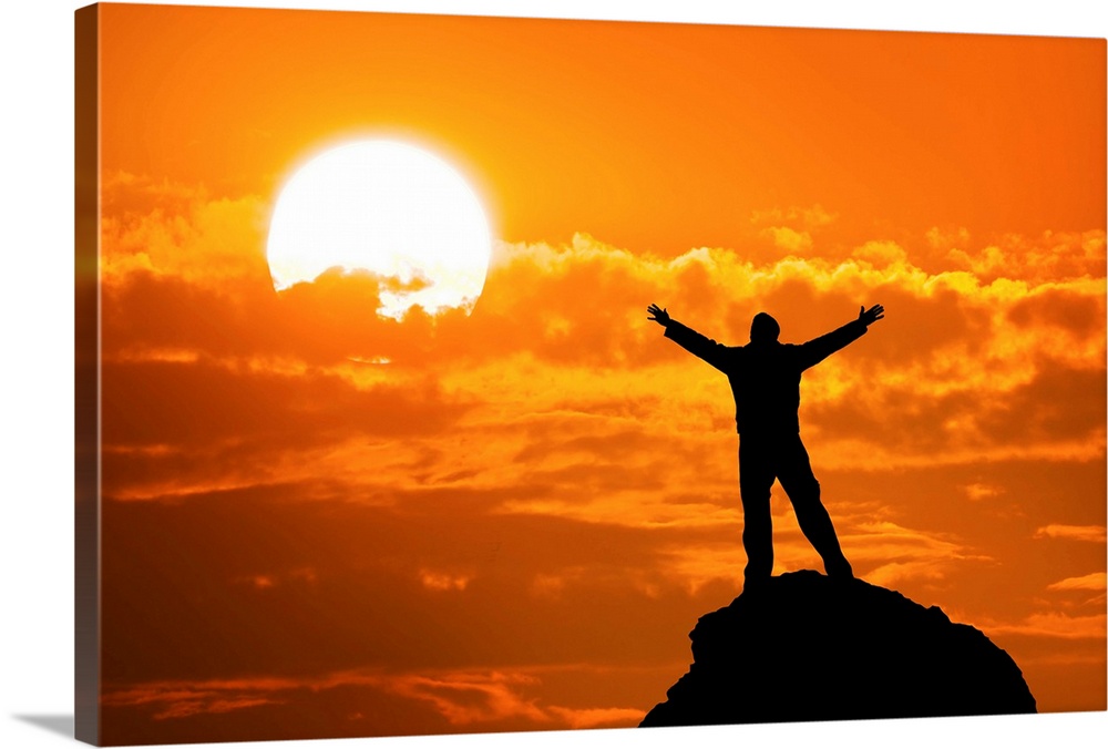Silhouette of man on mountain peak with arms outstretched looking at the sun