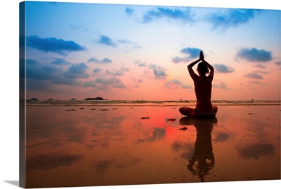Silhouette of woman practicing yoga on the beach at sunset
