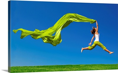 Young woman jumping on a green meadow with a green scarf