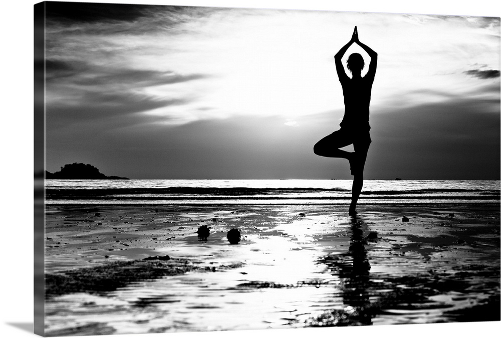 Black and white picture: Young woman practicing yoga on the beach at sunset.