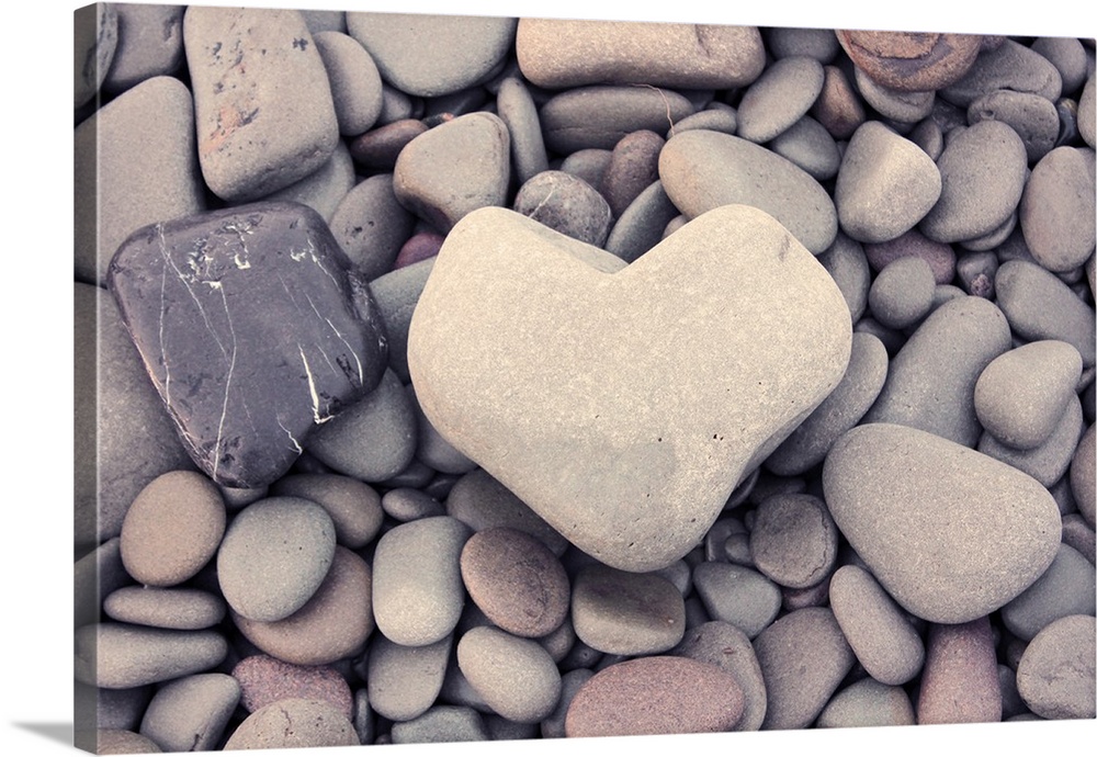 A smooth stone in the shape of a heart on a bed of round pebbles.