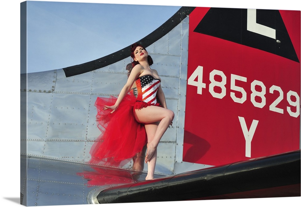 Beautiful 1940's style pin-up girl standing on the tail of a B-17 bomber.